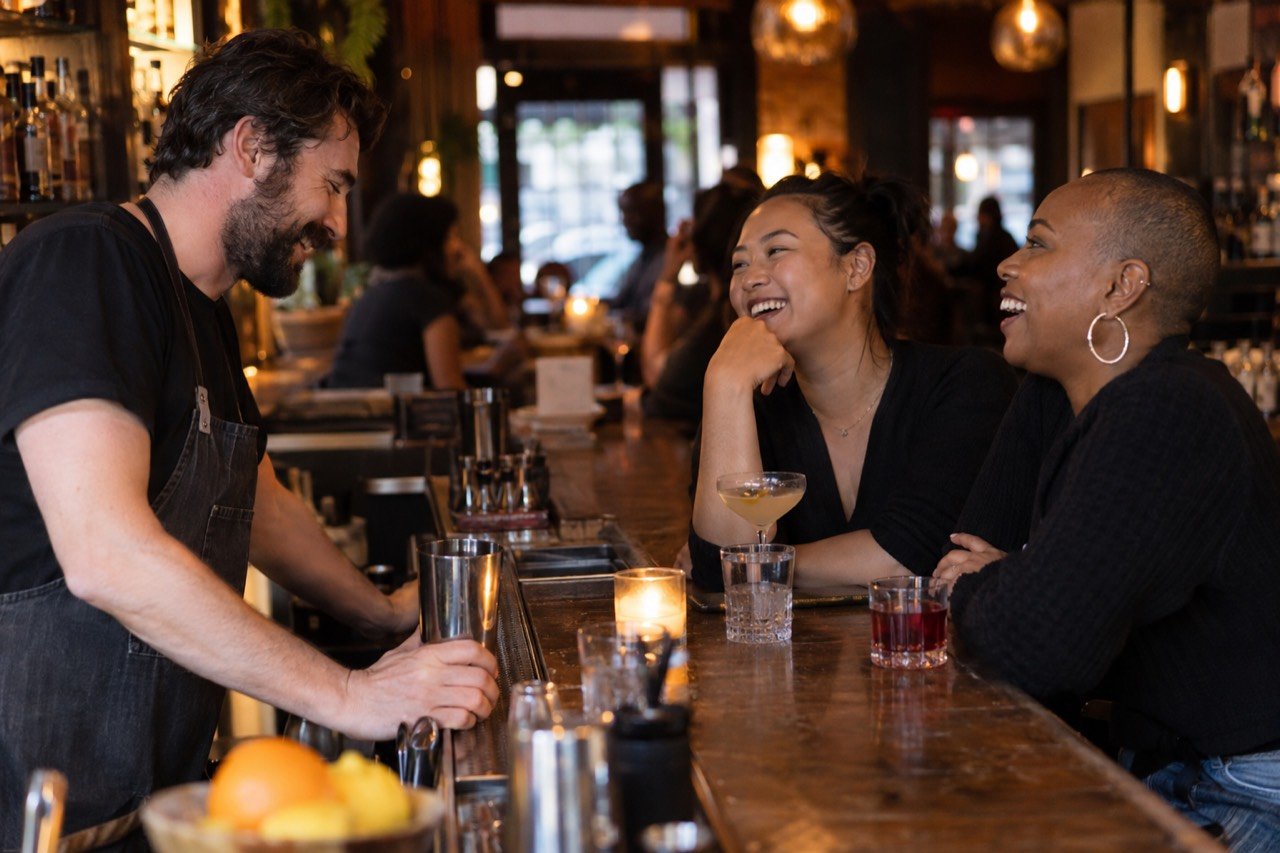 A bartender laughs with regulars at a neighborhood bar