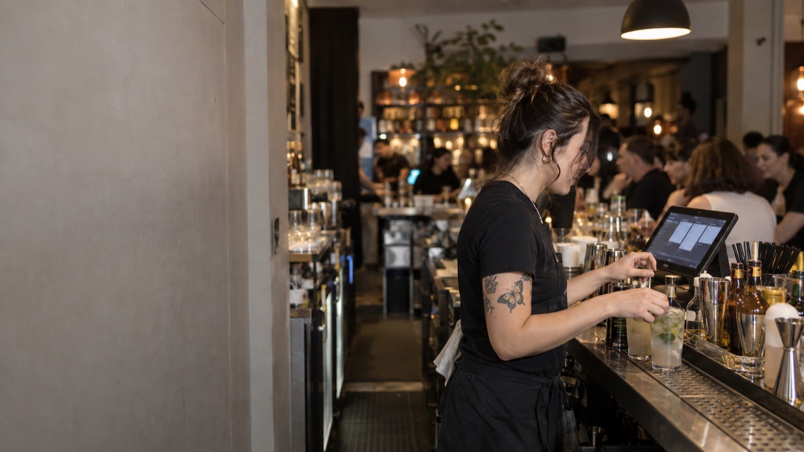 A bartender reads a written-out order on the tablet behind the bar before making it