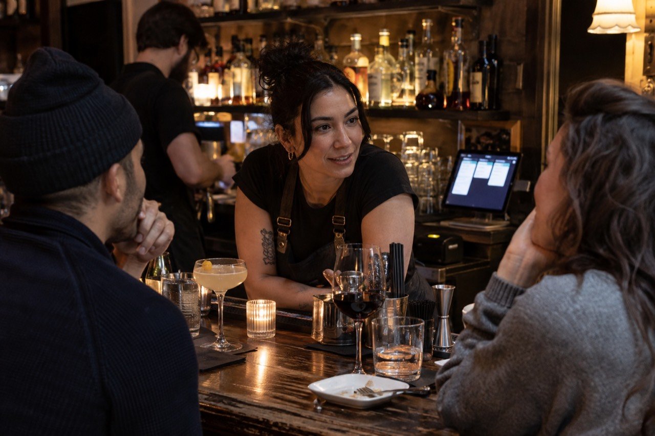 A bartender at an NYC bar chats with regulars while a new order arrives on the tablet behind the bar