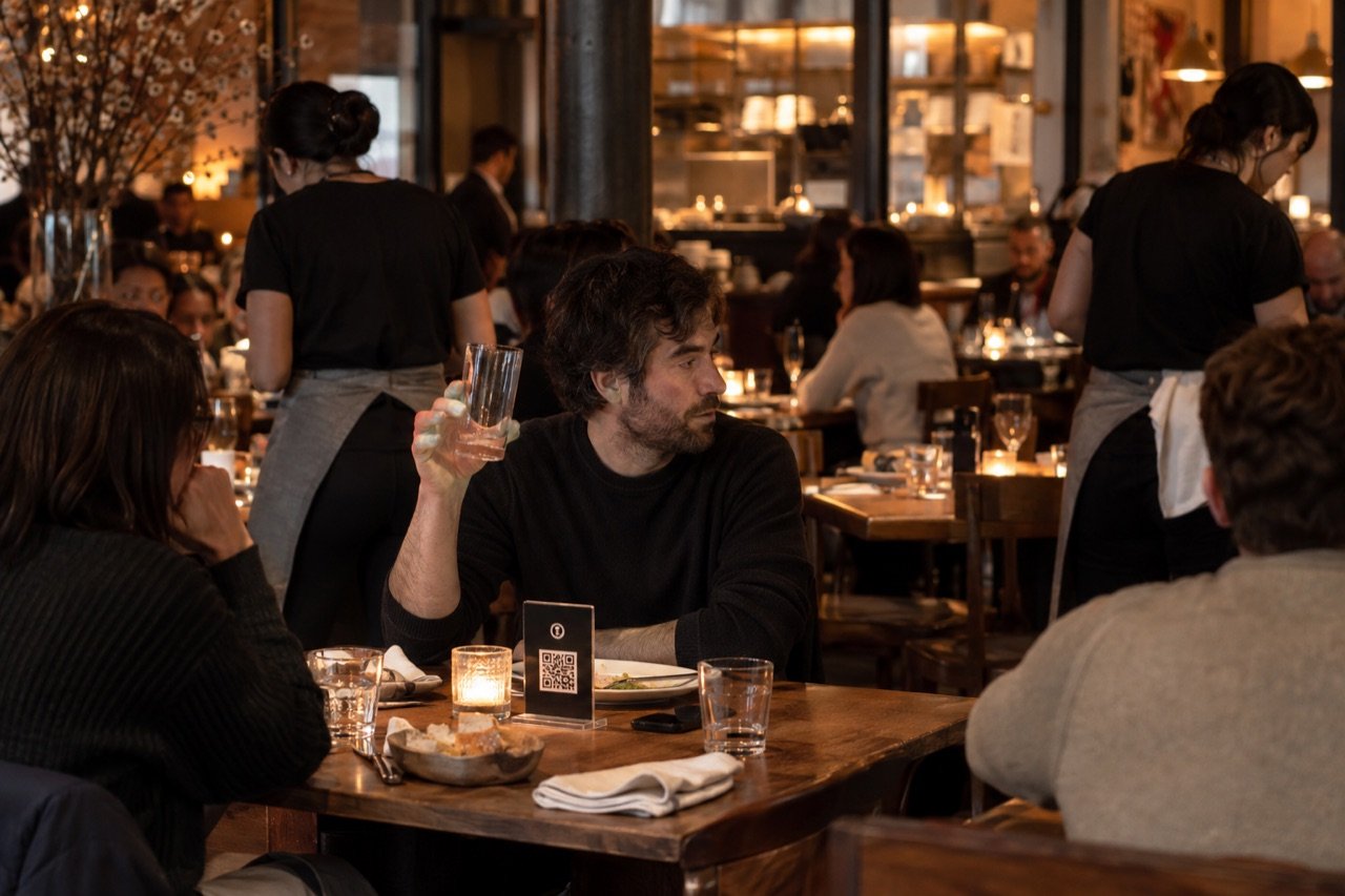 A diner raises a hand for a server who is busy at another table