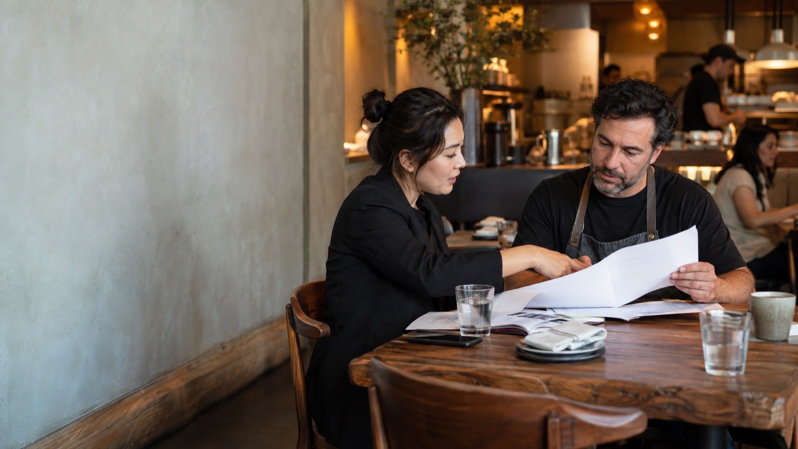 A hospitality consultant and a restaurant owner review a plan at a table
