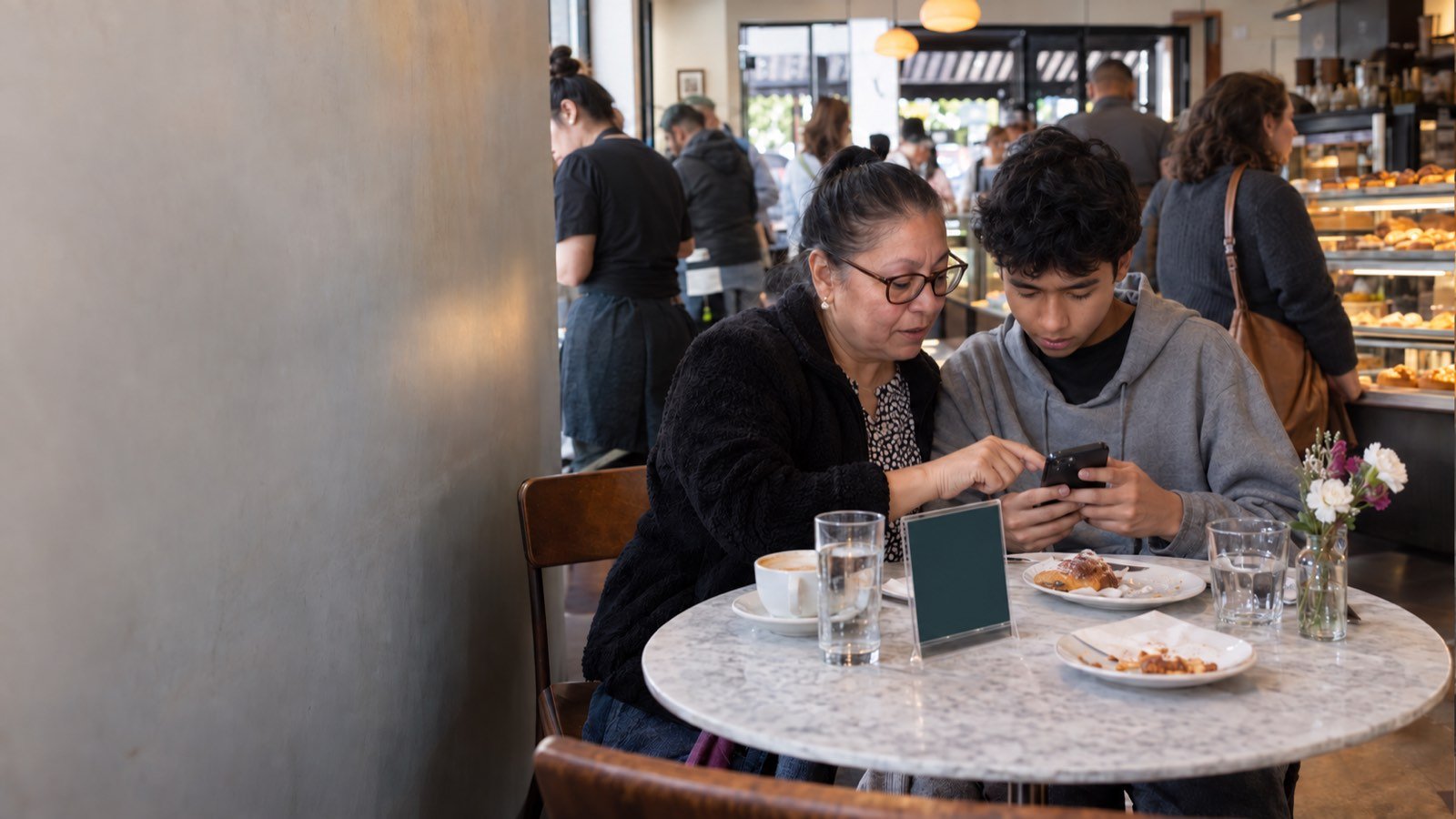 A family at a Queens café table orders by tapping the printed display, grandmother and grandson reading the menu together