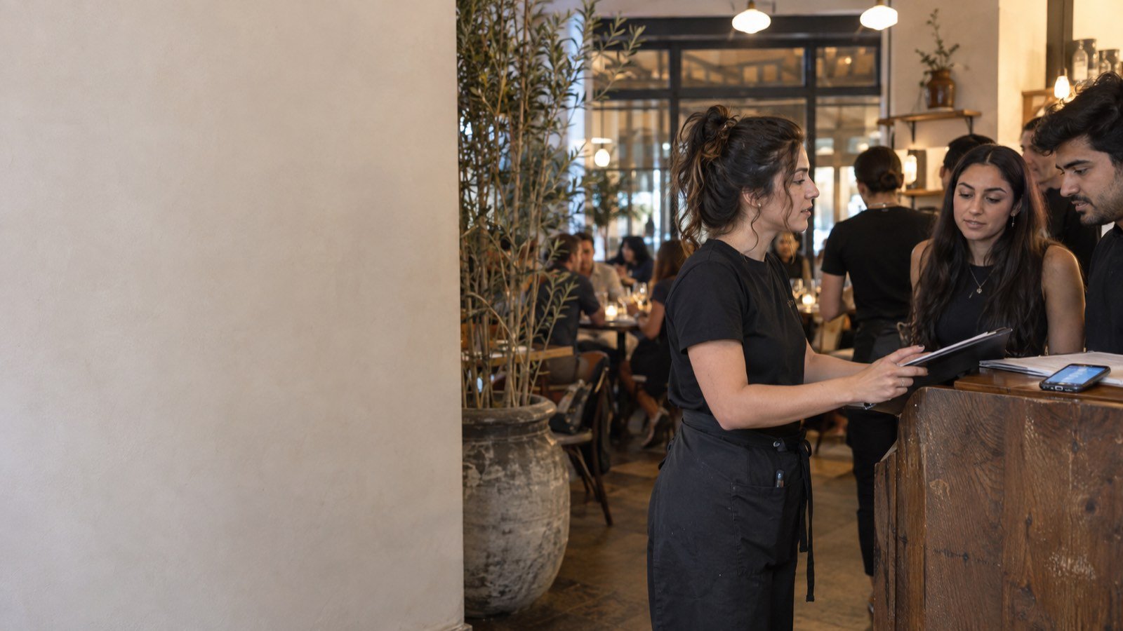 A restaurant phone rings at the host stand while staff are busy with a full room