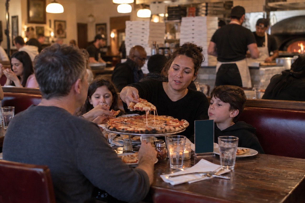 A pizzeria counter with pickup boxes and booths full of families