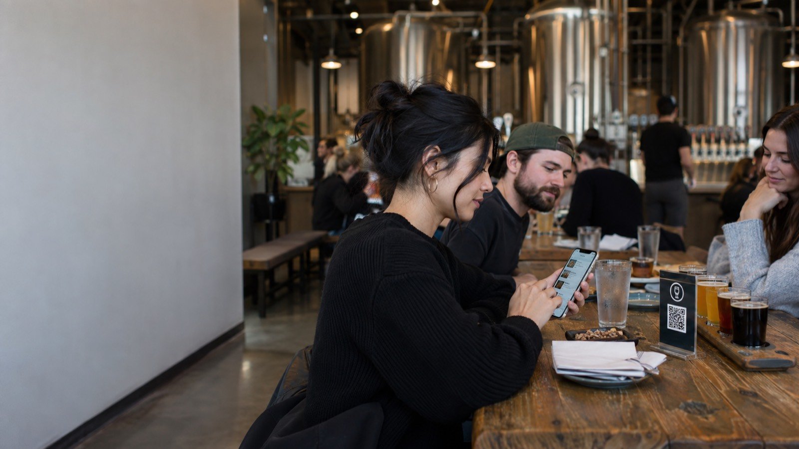 Friends at a long taproom table order the next round by tapping the printed display
